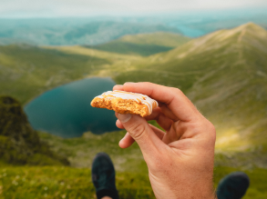 一个人拿着零食的特写，他们的脚在山和湖的背景